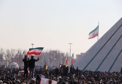 Two men holding Iranian flag beside Azadi Tower