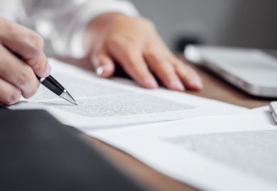 A hand clasps a pen, writing on a document A hand clasps a pen, writing on a document