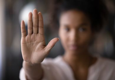 A woman holds her hand up in front of her to signal 'no' A woman holds her hand up in front of her to signal 'no'