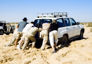 People pushing car stuck in sand