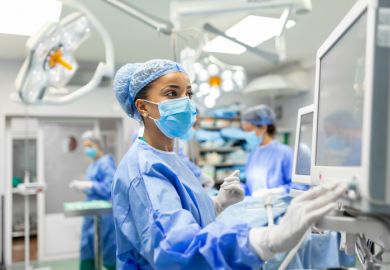 Anesthetist Working In Operating Theatre Wearing Protecive Gear checking monitors.