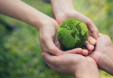 Two pairs of hands hold a tennis ball-sized green globe of the world