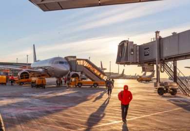 Front view big modern passenger aircraft approach boarding with stairs vehicle against airport building morning evening warm sun.