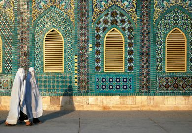 Two women wearing white burqas (burkas) walk past the Blue Mosque in Mazar-i-Sharif, Balkh Province, Afghanistan.
