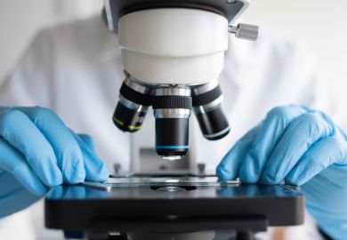 Researcher working with microscope wearing blue gloves