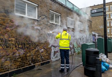 A Tower Hamlet Council worker cleaning graffiti off a building with a jet power wash.