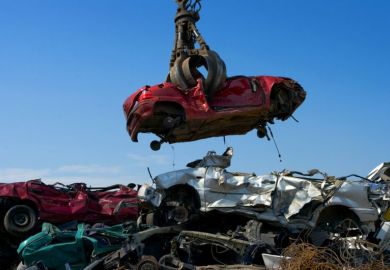 A shattered car is lowered into a pile of other crushed cars A shattered car is lowered into a pile of other crushed cars