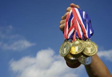 A hand holding a clutch of gold medals