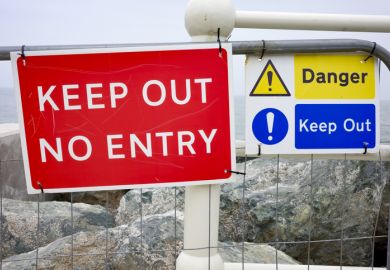 Red and blue 'Keep Out' signs on a fence by the sea