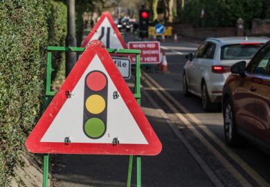 Traffic light road ahead sign against cars in the background.