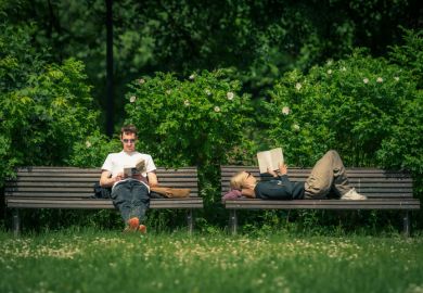 Couple sitting and reading a book on a bench in a public park in summer Couple sitting and reading a book on a bench in a public park in summer