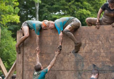 Team of people help each other tackle a high slippery wooden barrier on their gruelling 12 mile assault course