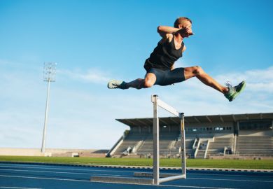 oung athlete jumping over a hurdle during training on racetrack in athletics stadium.