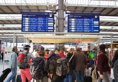  Several people waiting in a train station for their train with the destination board in the background