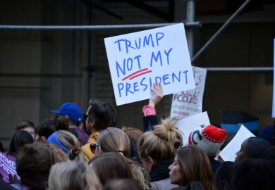 Someone in a crowd holds up a sign saying 'Trump - not my president'