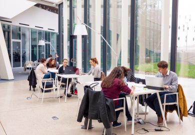 Young adult students sitting in groups in modern library and studying.