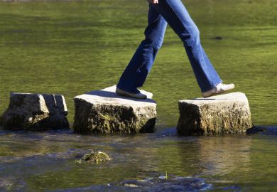 A person crossing three stepping stones on a river 