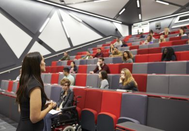 A woman lectures to a half-empty lecture theatre