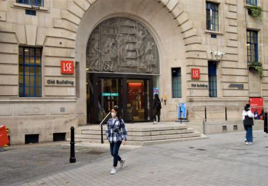 London, United Kingdom - November 13 2020 A student wearing a protective face mask walks past the LSE Old Building, London School of Economics and Political Science.