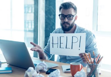 Man at desk holding 'Help' sign