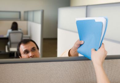 Man handing file/documents to colleague over office partition