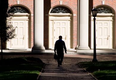 A man hidden in shadows walking towards entrance of building. To illustrate that staff accused of sexual harassment are free to leave their position and gain a new job at a different institution with no obligation to disclose any allegations.