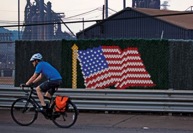 Man riding bicycle past United States of America flag