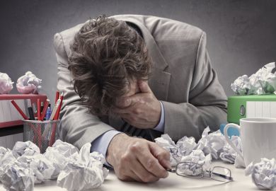 Man with head in hand surrounded by paper