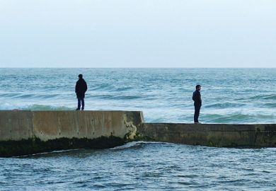 Men standing in opposite directions on seafront wall Men standing in opposite directions on seafront wall