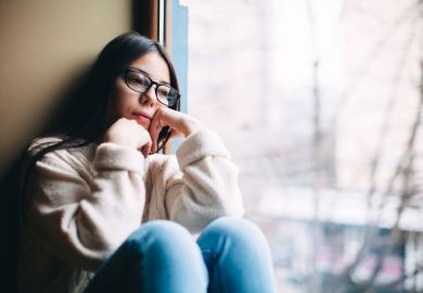 A woman sits by a window looking sad