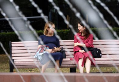 Moscow, Russia - August 2022 Two women talking while sitting on wooden bench in Moscow park, hot weather in summer city