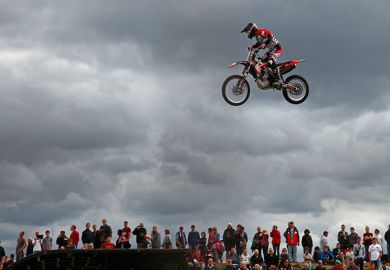Person on a motorbike jumping above crowd of spectators. To illustrate wages rising faster at universities outside national bargaining.