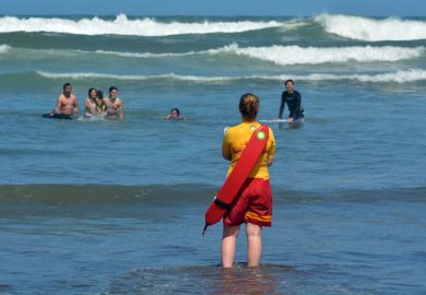 Muriwai, New Zealand - January 2 2015 New Zealand woman Lifeguard on duty watches swimmers in the sea.