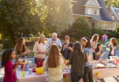 Neighbours talk and eat around a table at a block party representing collaboration between neighbouring universities