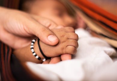 newborn baby holding the parent hand while sleeping at cradle