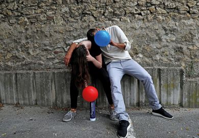 Two young people inhale nitrous oxide from balloons