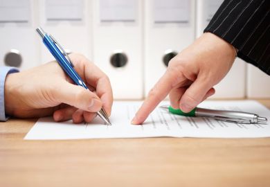 A person in a suit points to where to sign on a document