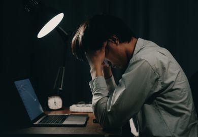 A man working on a laptop holds his head late at night A man working on a laptop holds his head late at night, illustrating overwork