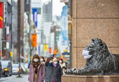 pedestrians walking past masked statue Tokyo