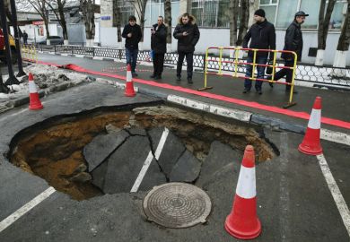 People looking at sinkhole in road People looking at sinkhole in road