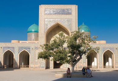 People sitting in the shade of a tree near a mosque, Uzbekistan. To illustrate branch campuses being set up in the country.