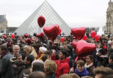 People with red heart balloons outside the Louvre