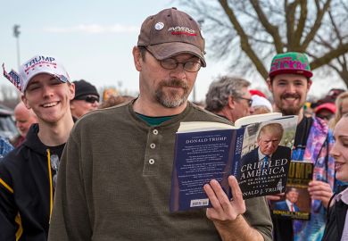 A man reads a Donald Trump book while waiting in a long line for admission to a Trump campaign rally, 2016. To illustrate that academics might need to 'tread carefully' with courses on Trump.