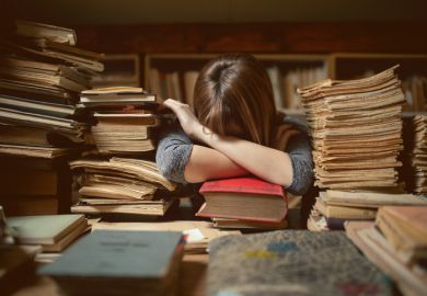 A young researcher with her head on her desk surrounded by piles of documents, illustrating early-career overwork