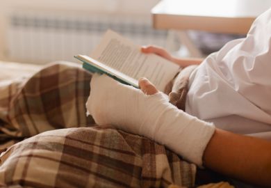 A person reads a book with a bandaged arm, symbolising the scarring PhD experience
