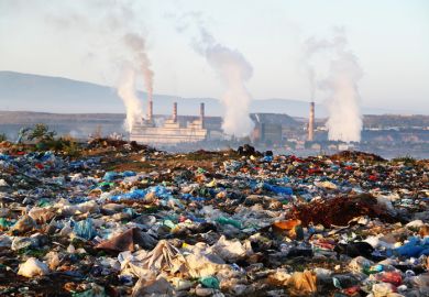 Factory chimneys behind a rubbish dump, illustrating exploitative capitalism