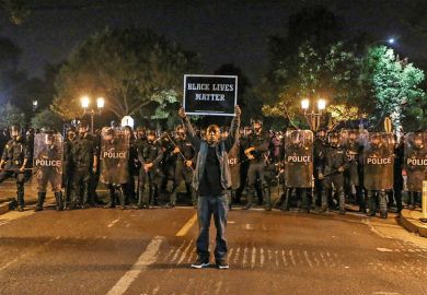 A man holds a placard saying ‘Black Lives Matter’ before a line of policemen A man holds a placard saying ‘Black Lives Matter’ before a line of policemen
