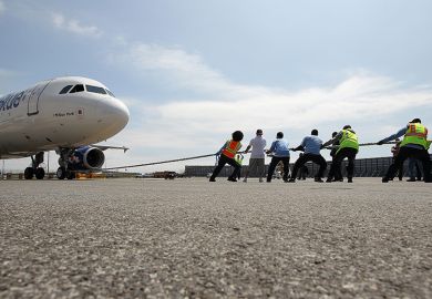 A team of people try to pull a 150,000 pound aircraft, illustrating the extra burden on universities from the UK government’s proposed levy on international student fees.