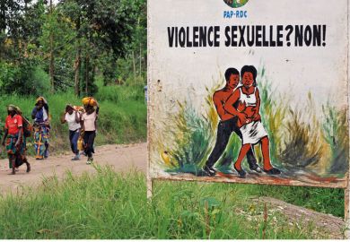 Congolese women walk past a sign opposing sexual violence Congolese women walk past a sign opposing sexual violence