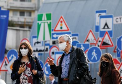 People in face masks in front of signs